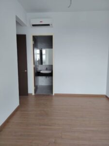 Empty room with light wood floor and white walls, doorway to small bathroom with sink and mirror; wall AC unit mounted above the door.
