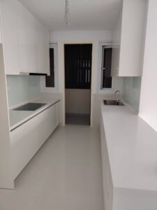 Modern white kitchen with glossy cabinets, a built-in cooktop on the left, glass backsplash, and a long white countertop running along the right side toward a doorway at the back.
